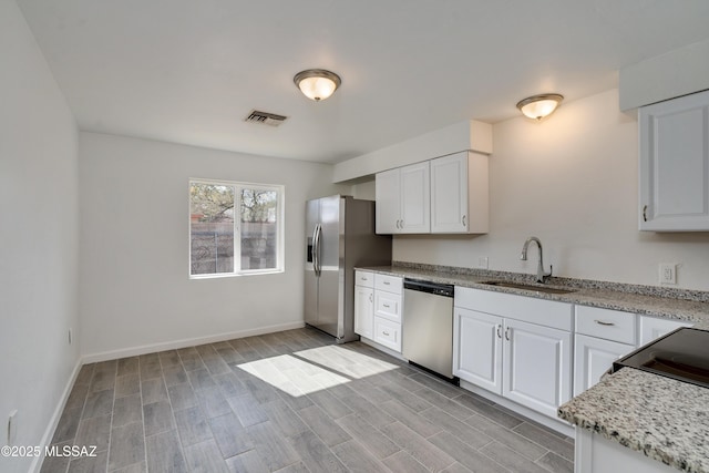 kitchen with light stone counters, appliances with stainless steel finishes, sink, and white cabinets