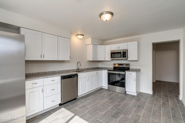 kitchen featuring stainless steel appliances, white cabinetry, light stone countertops, and sink