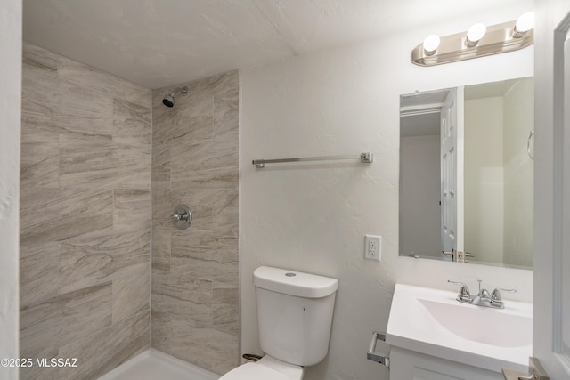 bathroom with vanity, tiled shower, and toilet