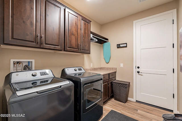 clothes washing area featuring washer and clothes dryer, cabinets, and light wood-type flooring