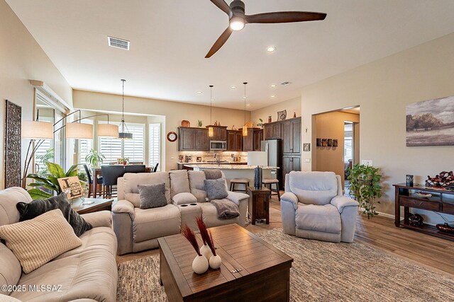 kitchen with sink, appliances with stainless steel finishes, a kitchen island with sink, hanging light fixtures, and light stone countertops