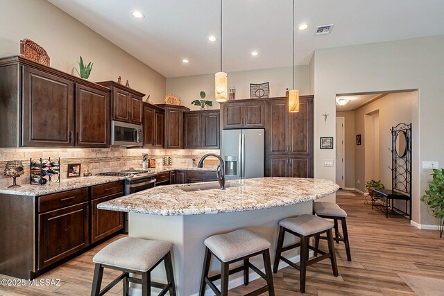 kitchen with dark brown cabinets, light stone counters, stainless steel fridge, and backsplash