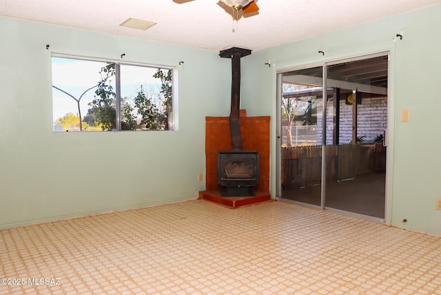 unfurnished living room with ceiling fan and a wood stove