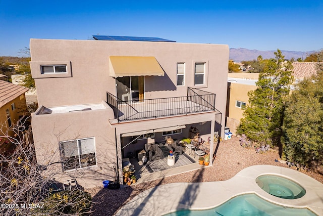 back of house featuring a mountain view, a patio, a balcony, and an in ground hot tub