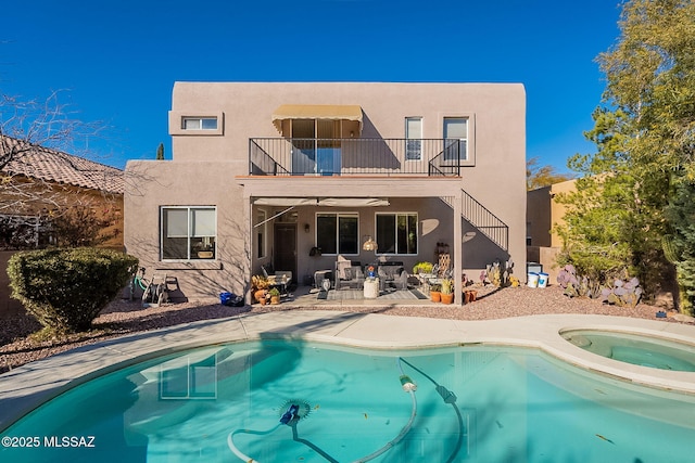 rear view of property featuring a patio, a balcony, and a pool with hot tub