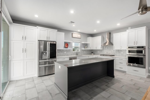 kitchen featuring tasteful backsplash, white cabinetry, a center island, stainless steel appliances, and wall chimney exhaust hood