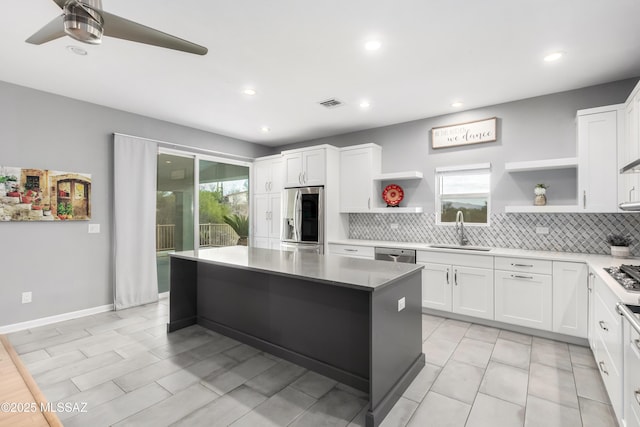 kitchen featuring stainless steel appliances, white cabinetry, a kitchen island, and sink