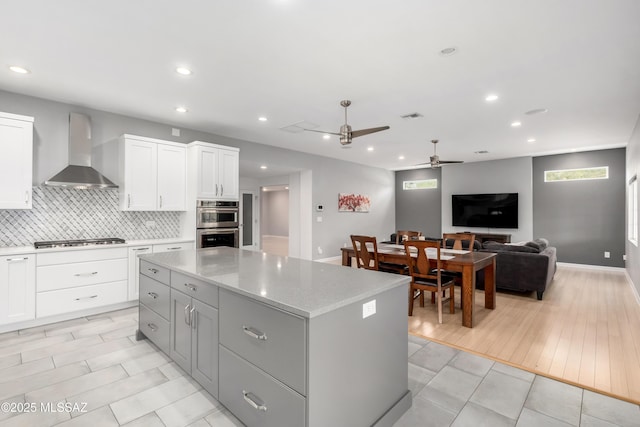 kitchen with wall chimney exhaust hood, a center island, stainless steel appliances, decorative backsplash, and white cabinets