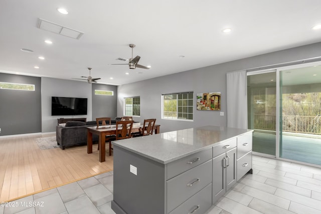 kitchen featuring gray cabinets, a kitchen island, light stone counters, and ceiling fan