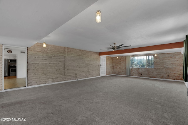 carpeted spare room with ceiling fan and brick wall