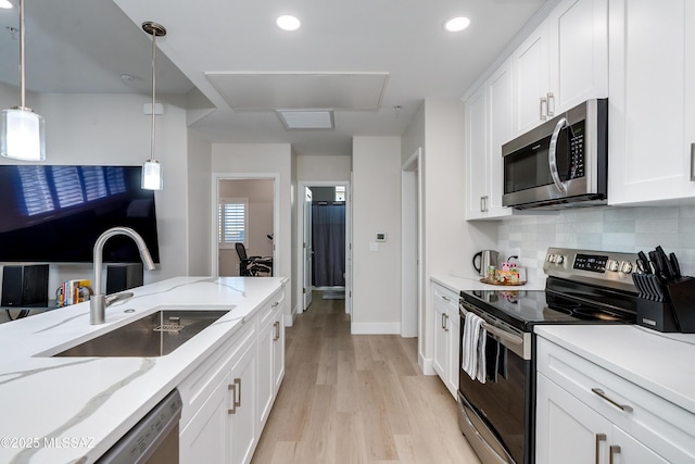 kitchen with appliances with stainless steel finishes, sink, white cabinets, hanging light fixtures, and light stone counters