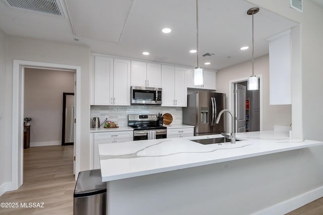 kitchen with pendant lighting, stainless steel appliances, kitchen peninsula, and white cabinets