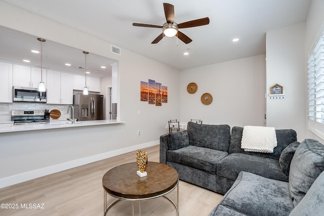 living room with sink, ceiling fan, and light wood-type flooring