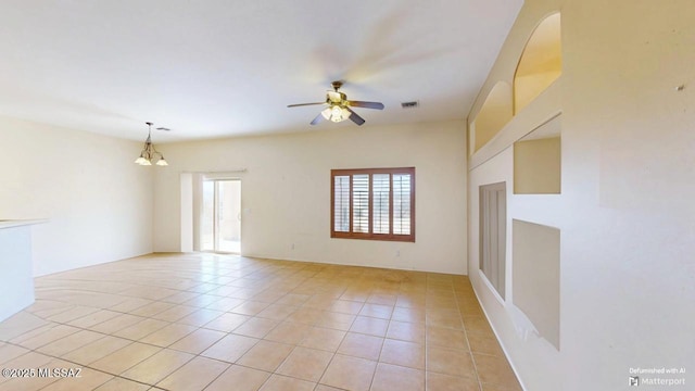 empty room with light tile patterned floors, visible vents, and ceiling fan with notable chandelier