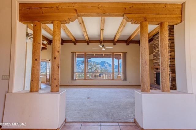 unfurnished living room with ceiling fan, a large fireplace, light carpet, and beam ceiling