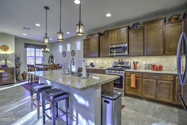 kitchen with pendant lighting, sink, appliances with stainless steel finishes, tasteful backsplash, and an island with sink