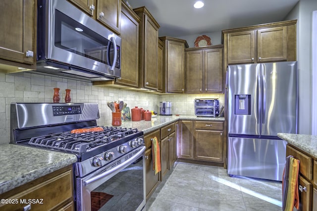 kitchen with stainless steel appliances, light stone countertops, light tile patterned floors, and decorative backsplash