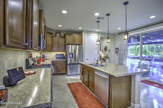 kitchen featuring sink, appliances with stainless steel finishes, pendant lighting, a kitchen island with sink, and backsplash