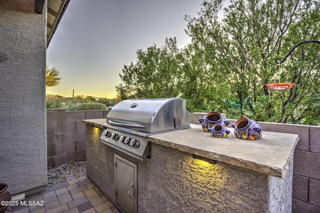 patio terrace at dusk with an outdoor kitchen and area for grilling