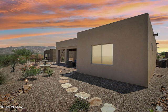 property exterior at dusk with a mountain view, central AC unit, and a patio area