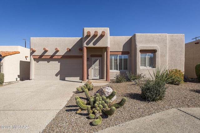 pueblo-style house with concrete driveway, an attached garage, and stucco siding