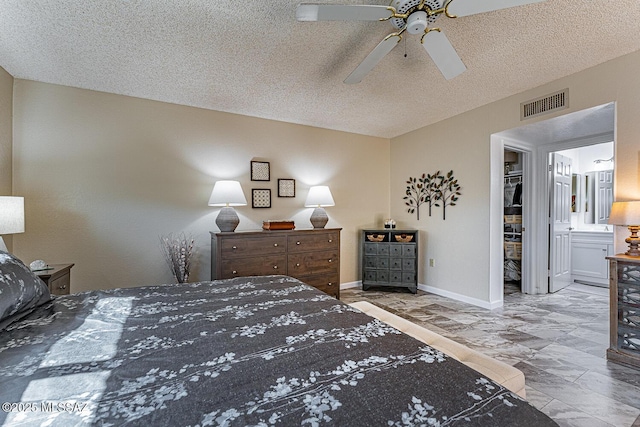 bedroom featuring ceiling fan, a walk in closet, ensuite bathroom, and a textured ceiling