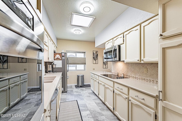 kitchen with tasteful backsplash, appliances with stainless steel finishes, cream cabinets, and a textured ceiling