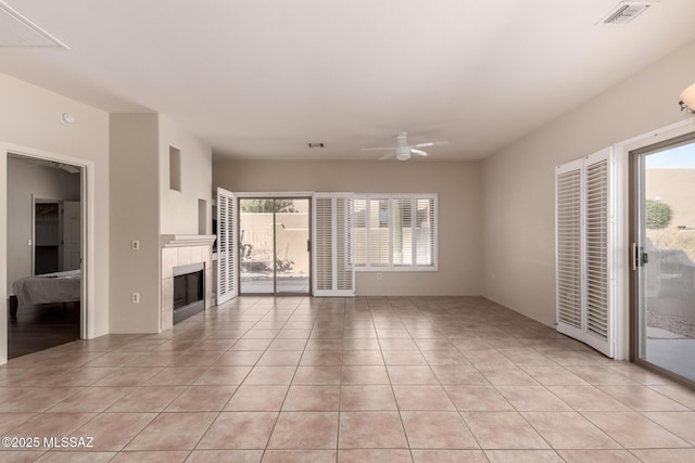 unfurnished living room featuring a tiled fireplace, a healthy amount of sunlight, light tile patterned floors, and ceiling fan