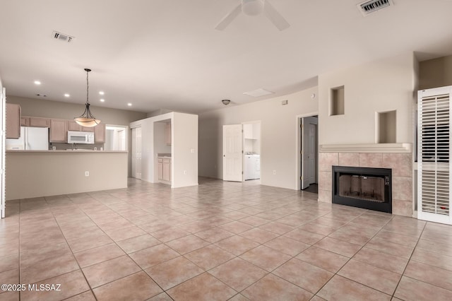 unfurnished living room with light tile patterned flooring, ceiling fan, washer / clothes dryer, and a tiled fireplace