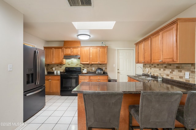 kitchen with electric range, a skylight, a kitchen breakfast bar, stainless steel refrigerator with ice dispenser, and kitchen peninsula