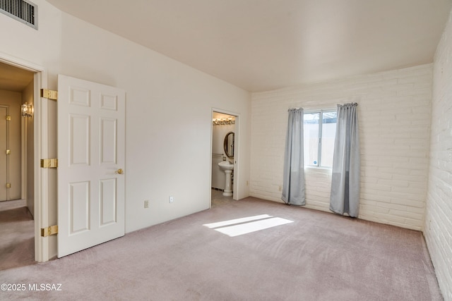 unfurnished bedroom with connected bathroom, light colored carpet, and brick wall