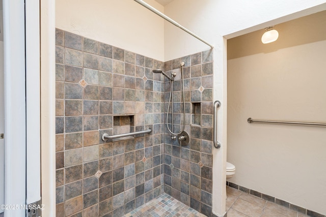 bathroom with tile patterned flooring, toilet, and tiled shower