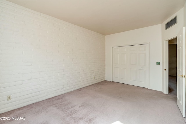 unfurnished bedroom with light carpet, a closet, and brick wall