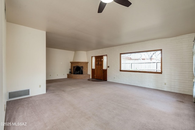 unfurnished living room featuring ceiling fan, a large fireplace, brick wall, and carpet