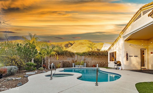 pool at dusk with an in ground hot tub, a mountain view, and a patio area