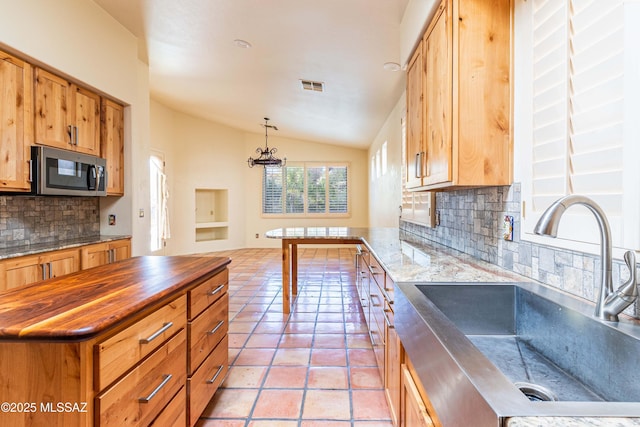 kitchen with wood counters, sink, vaulted ceiling, hanging light fixtures, and light tile patterned floors