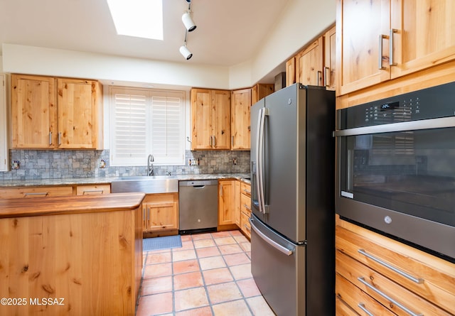 kitchen featuring sink, light tile patterned floors, appliances with stainless steel finishes, a skylight, and decorative backsplash