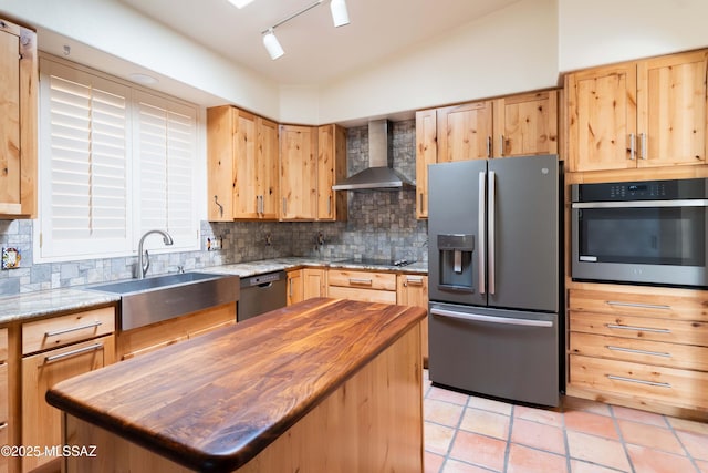 kitchen with wood counters, wall chimney exhaust hood, sink, a kitchen island, and black appliances