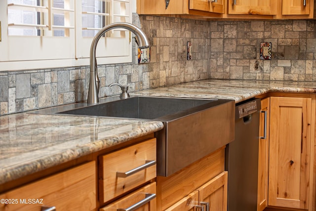 kitchen featuring tasteful backsplash, black dishwasher, sink, and light stone counters