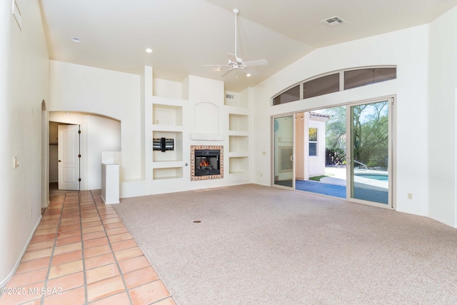 unfurnished living room featuring a brick fireplace, light colored carpet, built in features, and ceiling fan