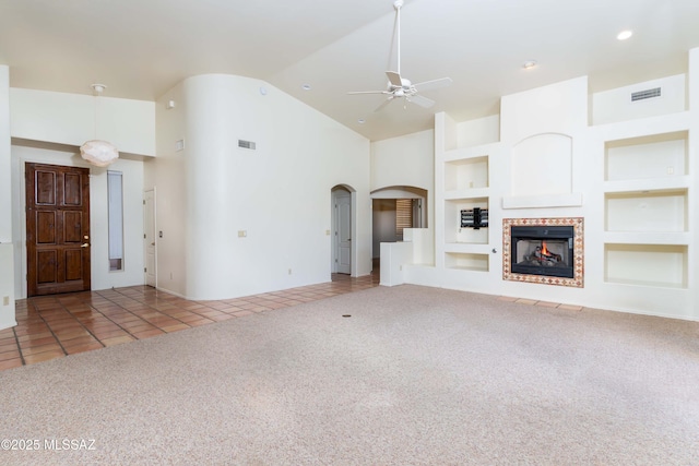 unfurnished living room featuring ceiling fan, high vaulted ceiling, a fireplace, light carpet, and built in shelves