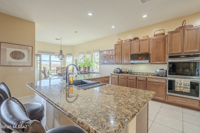 kitchen with hanging light fixtures, a large island with sink, stainless steel double oven, and a kitchen bar