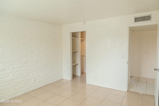 unfurnished bedroom featuring light tile patterned flooring, brick wall, and a spacious closet