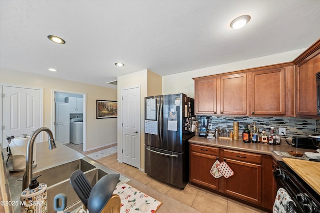 kitchen with black refrigerator, washer / clothes dryer, tasteful backsplash, sink, and range