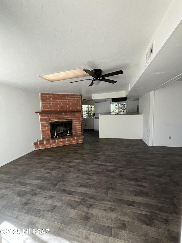 unfurnished living room featuring ceiling fan, dark hardwood / wood-style floors, a brick fireplace, and a textured ceiling