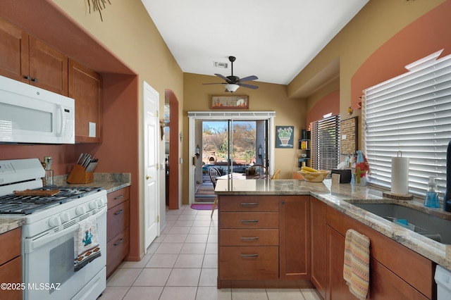 kitchen with light tile patterned flooring, sink, light stone counters, kitchen peninsula, and white appliances