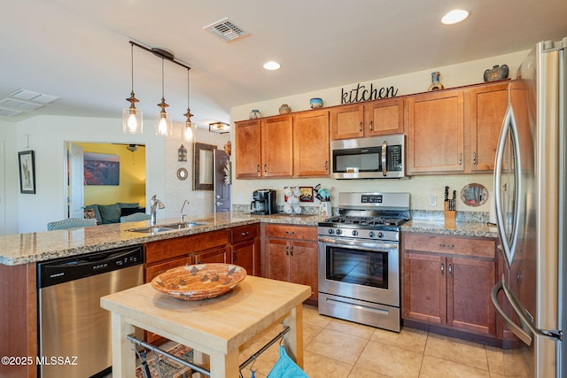 kitchen with sink, light stone counters, hanging light fixtures, appliances with stainless steel finishes, and kitchen peninsula