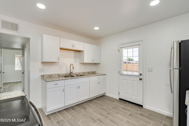 kitchen with white cabinetry, appliances with stainless steel finishes, sink, and light stone counters