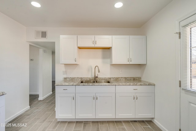 kitchen with sink, light stone countertops, and white cabinets