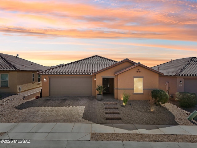 view of front facade featuring decorative driveway, a tiled roof, an attached garage, and stucco siding